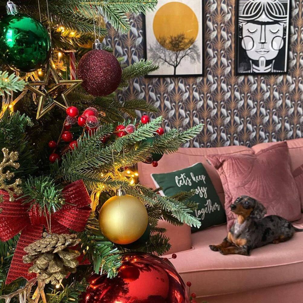 A festive style living rom with statement wallpaper, wall art, seasonal cushions and a decorated Christmas tree.
