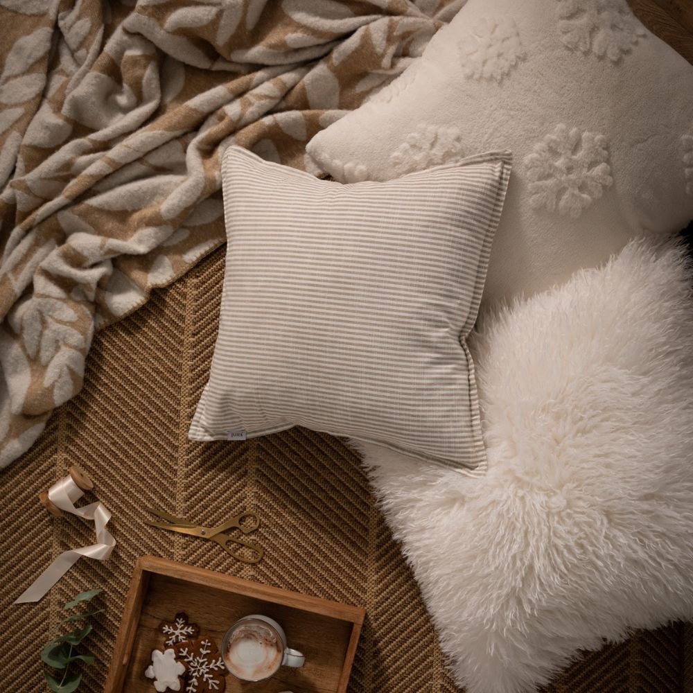 A Christmas set up with three fluffy cream cushions, a decorative brown woven throw and Christmas ribbon