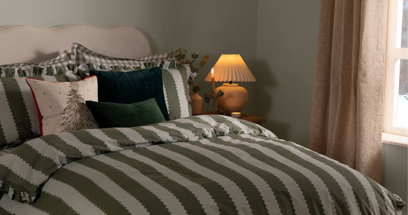 A bedroom with Christmas cushions and a green and light blue striped duvet cover.