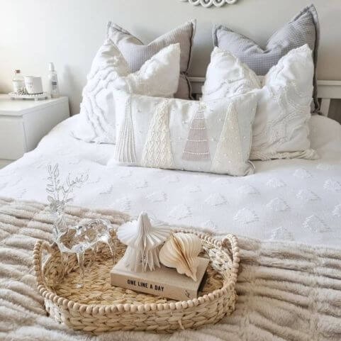 a neutral minimalist bedroom with white festive bedding, including a white duvet cover with a tufted tree design, embroidered and tufted scatter cushions, and a faux fur throw. 