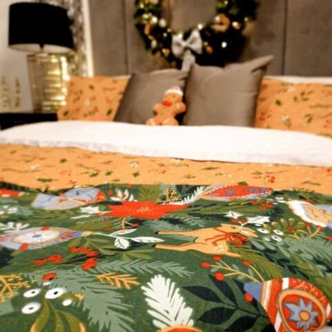 Green Christmas bedding with a traditional design of tree ornaments, made on a bed with matching pillowcases, grey scatter cushions, a gingerbread man plush toy and a festive wreath.