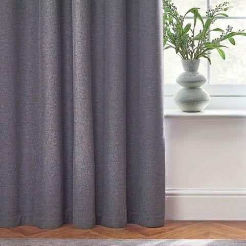 A grey blackout curtain panel hung in a white room, with a potted plant on the window sill.