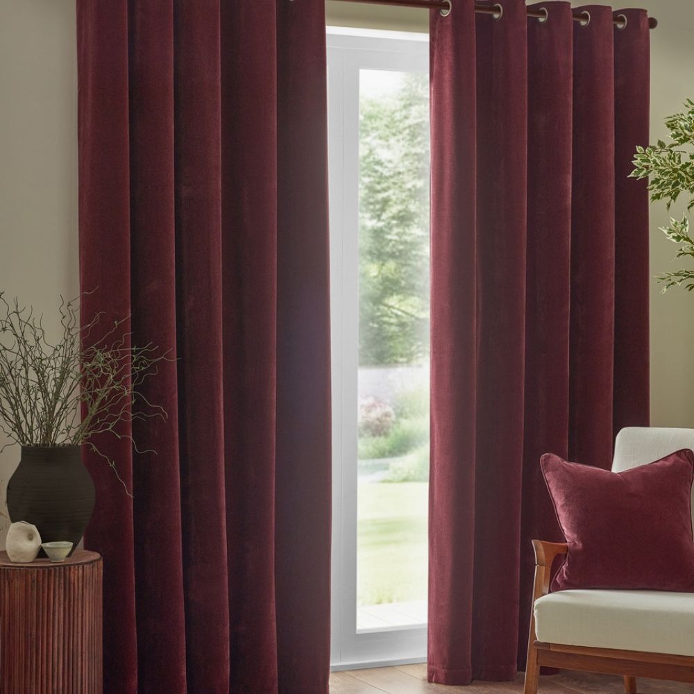 A pair of beetroot red curtains in chenille, with a matching cushion on a white arm chair
