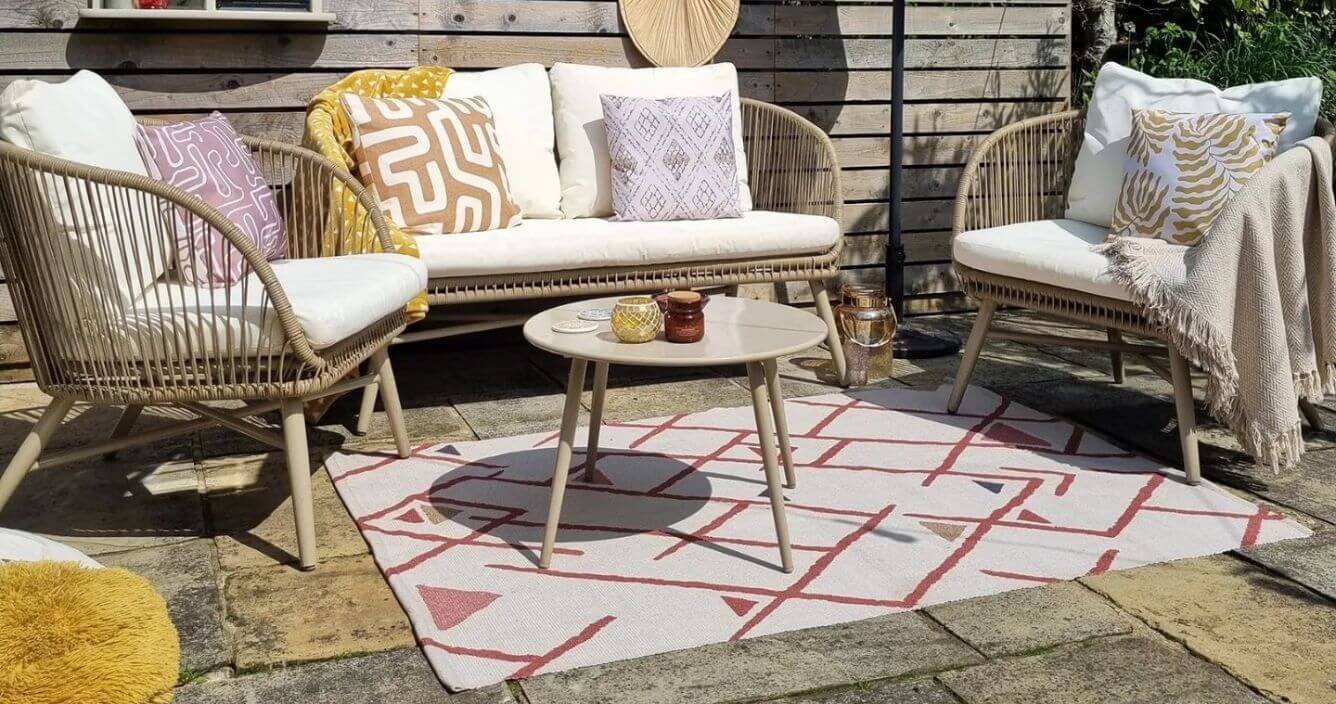 A patio decorated with a polyester outdoor rug, woven patio furniture, throws and weather-resistant outdoor cushions.