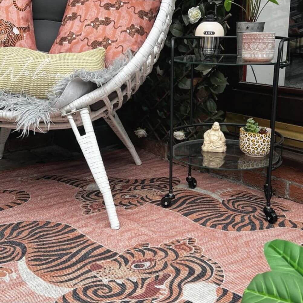 A polyester indoor/outdoor rug with a printed tibetan tiger design, laid underneath a white woven chair with coordinating outdoor cushions.