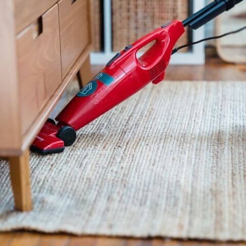A neutral woven rug with a plain design being cleaned with a small red vacuum.