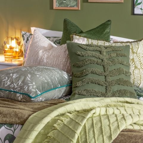 A selection of green and white scatter cushions with velvet, bouclé, tufted and printed designs, arranged on a floral duvet set in a biophilic style bedroom. 
