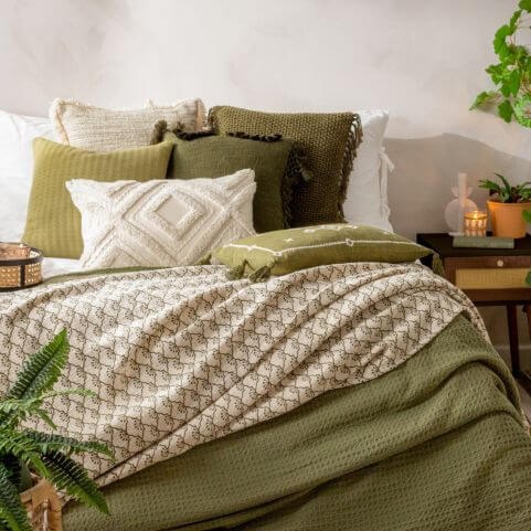 A boho biophilic style bedroom with a white duvet cover set, textured throws and a selection of earthy green and natural coloured scatter cushions.
