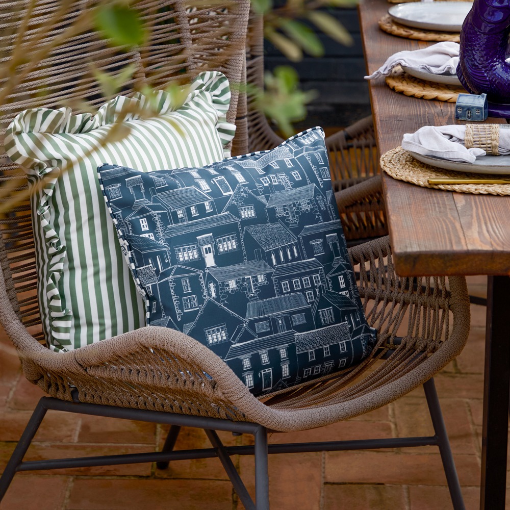 An outdoor cushion featuring a hand-painted coastal town design.
