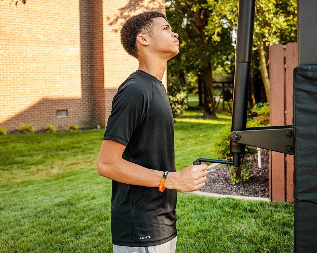 Basketball player using the actuator on an in-ground basketball hoop to raise or lower the rim