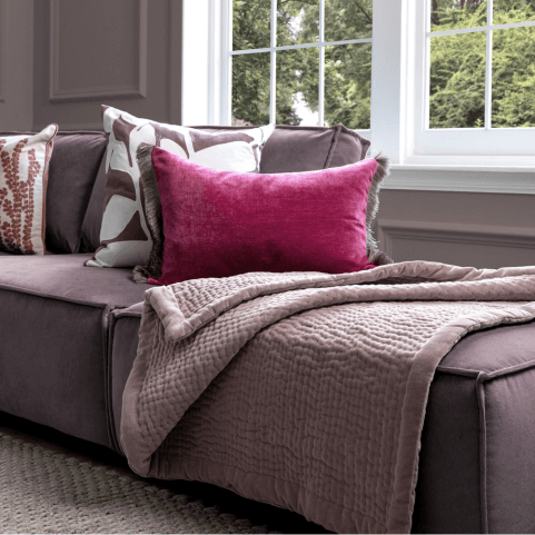 A selection of pink and grey sofa cushions arranged on a purple sofa.