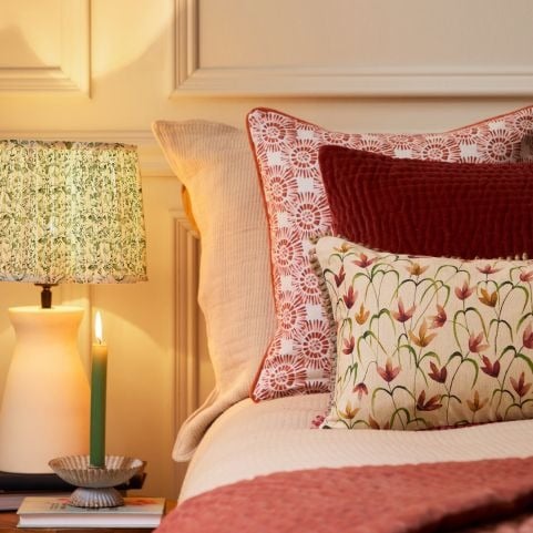A bed next to a bedside table with a table lamp and a candle stick