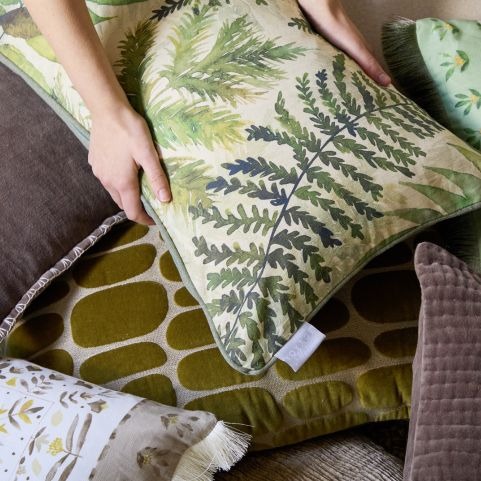 A zoomed in image of seasonal printed autumn cushions in shades of green featuring leafy designs