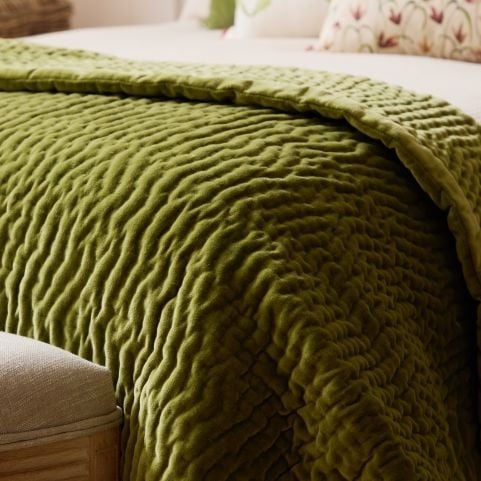 A thick velvet olive green throw blanket draped across the edge of a bed