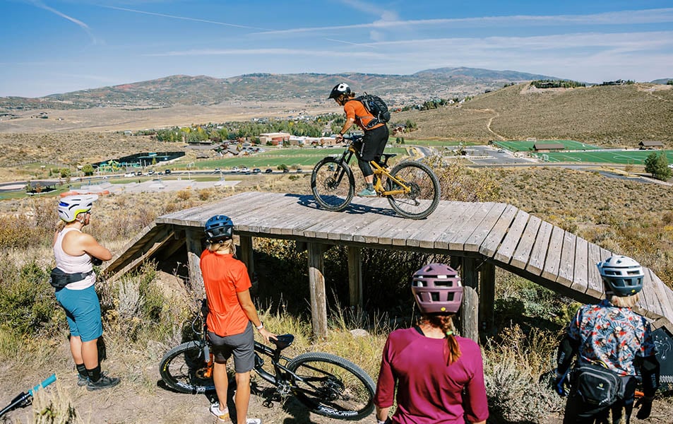 Women demonstrating how to ride a mountain bike over a wooden bridge