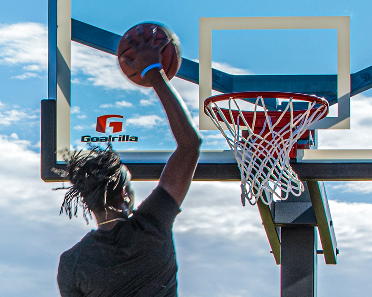 Basketball player with ball in palm going up to the basketball rim and net on a Goalrilla basketball hoop