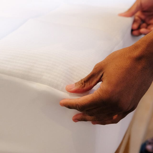 A close view of a man making his bed and fixing the corners on the Slumber Cloud Performance Mattress Pad