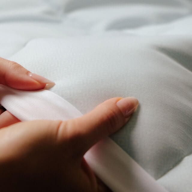 A detailed view of a woman touching the materials on the Slumber Cloud Essential Mattress Pad