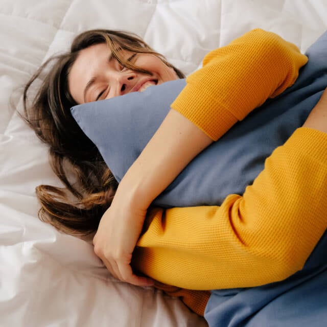 A woman lying in bed on a Slumber Cloud Down Comforter and clutching a pillow