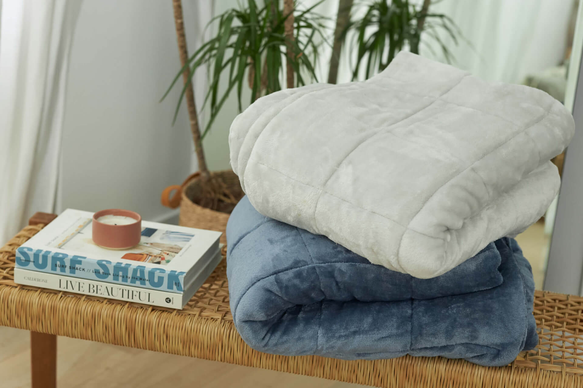 The Slumber Cloud Plush Throw in fog and bold blue folded and stacked on a wicker bench