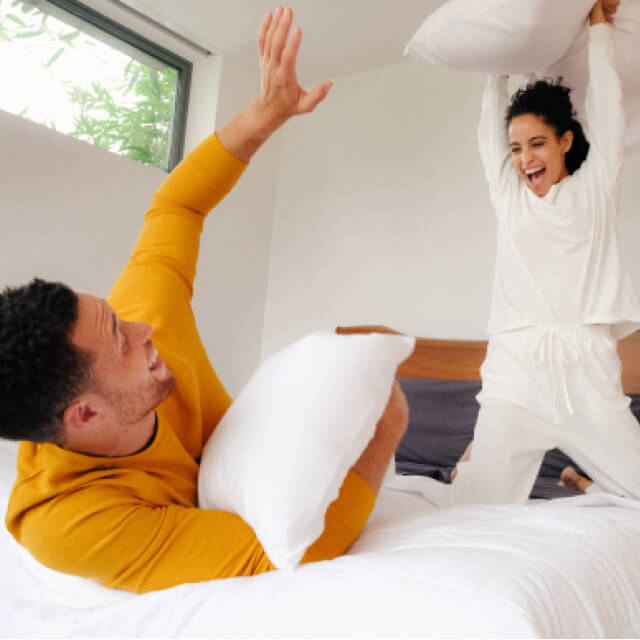 A man and woman pillow fighting in the morning on a bed fit with Slumber Cloud products