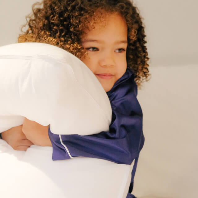 A child smiling and squeezing a Slumber Cloud Core Down Alternative Pillow