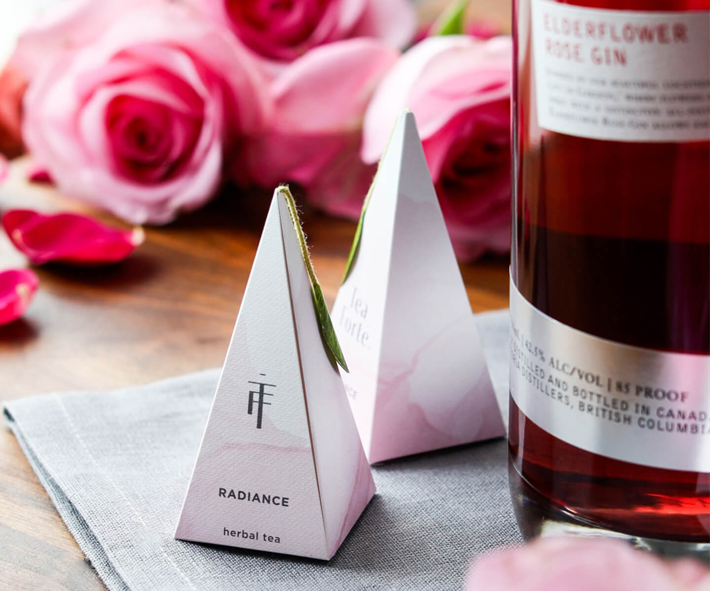 Radiance pyramid tea infuser closeup with roses and gin bottle on table in background. Photo by Emily Laurea.