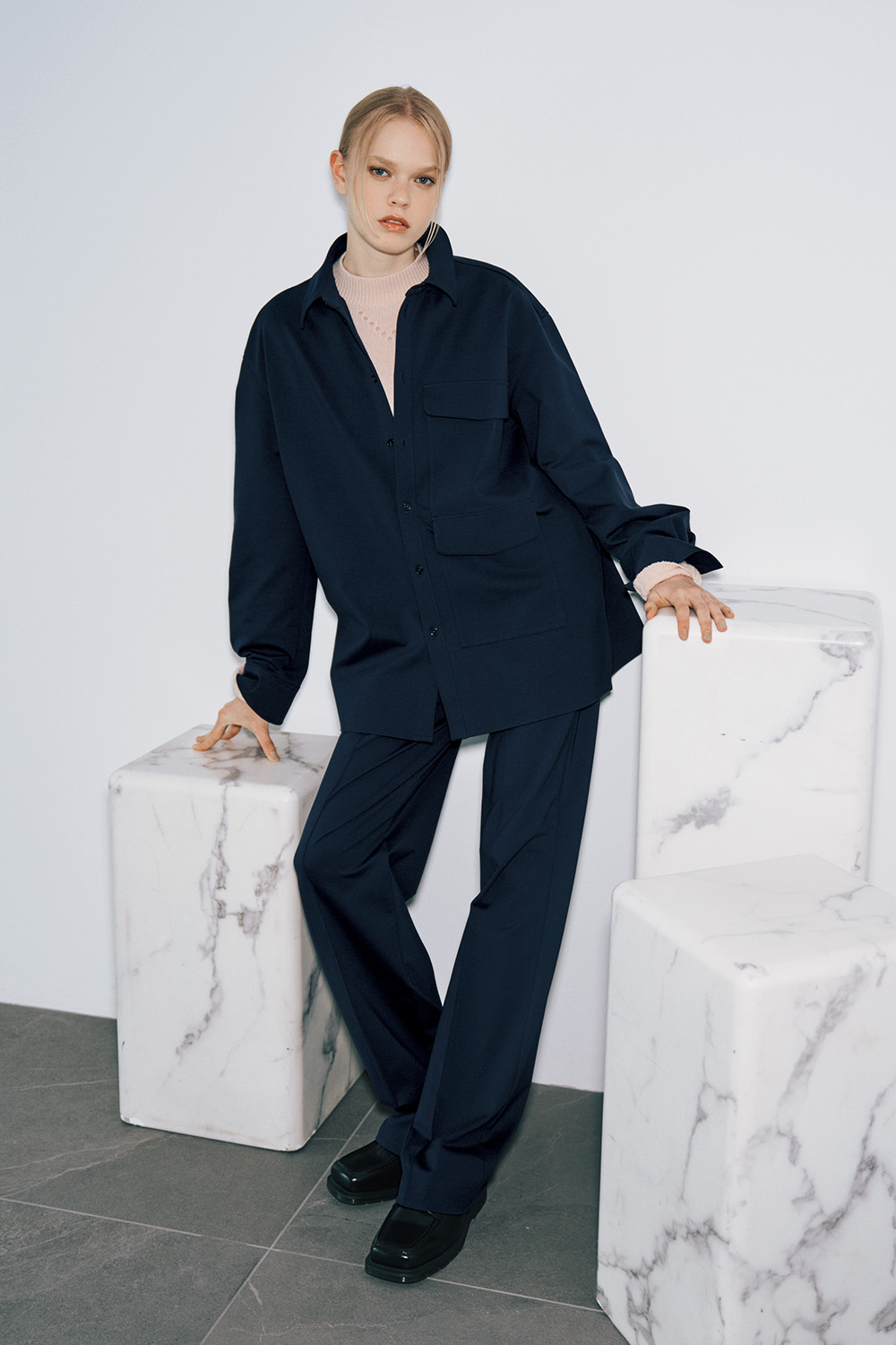 The model wears a navy oversized shirt jacket over a pale pink turtleneck, navy wide-leg trousers, and black leather loafers.
