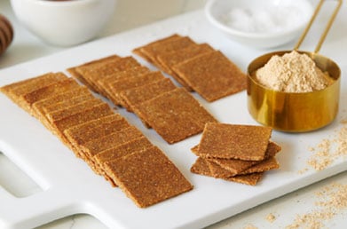 Homemade crackers made with Navitas Cauliflower Flour on a cutting board next to dip