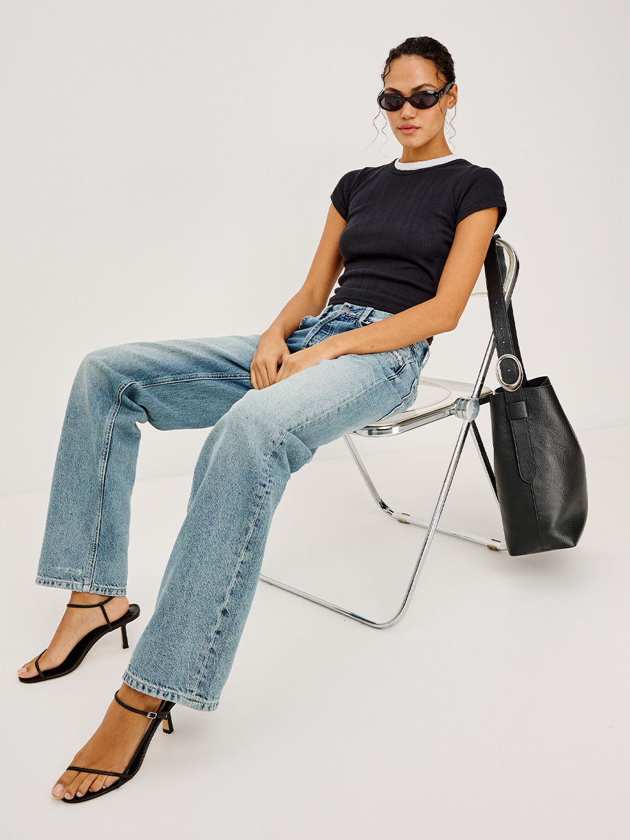 Seated woman wearing a t-shirt and jeans on white background. Click here to Shop All Denim