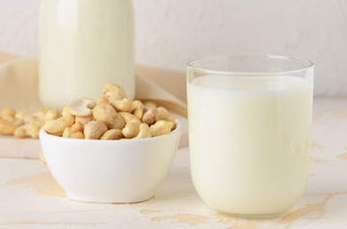 Glass of cashew milk made with Navitas Cashew Nuts next to a bowl of Navitas Cashew Nuts