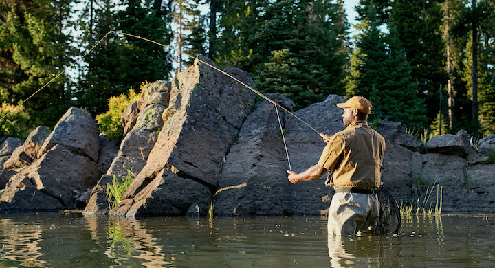 Load video: Man fishing in a lake wearing carhartt and rumpl