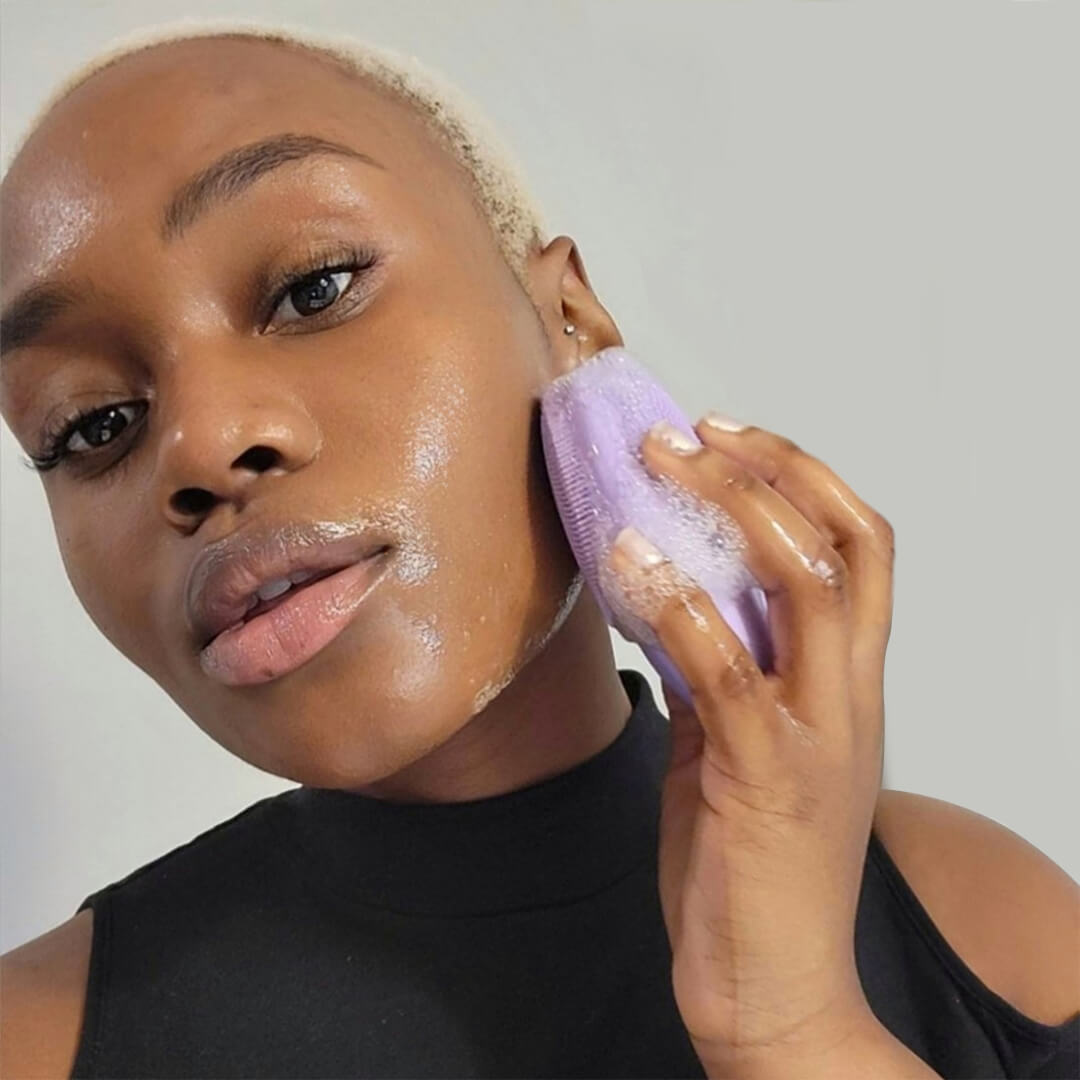 woman using the isla sonic facial cleansing brush in lavender to clean her skin