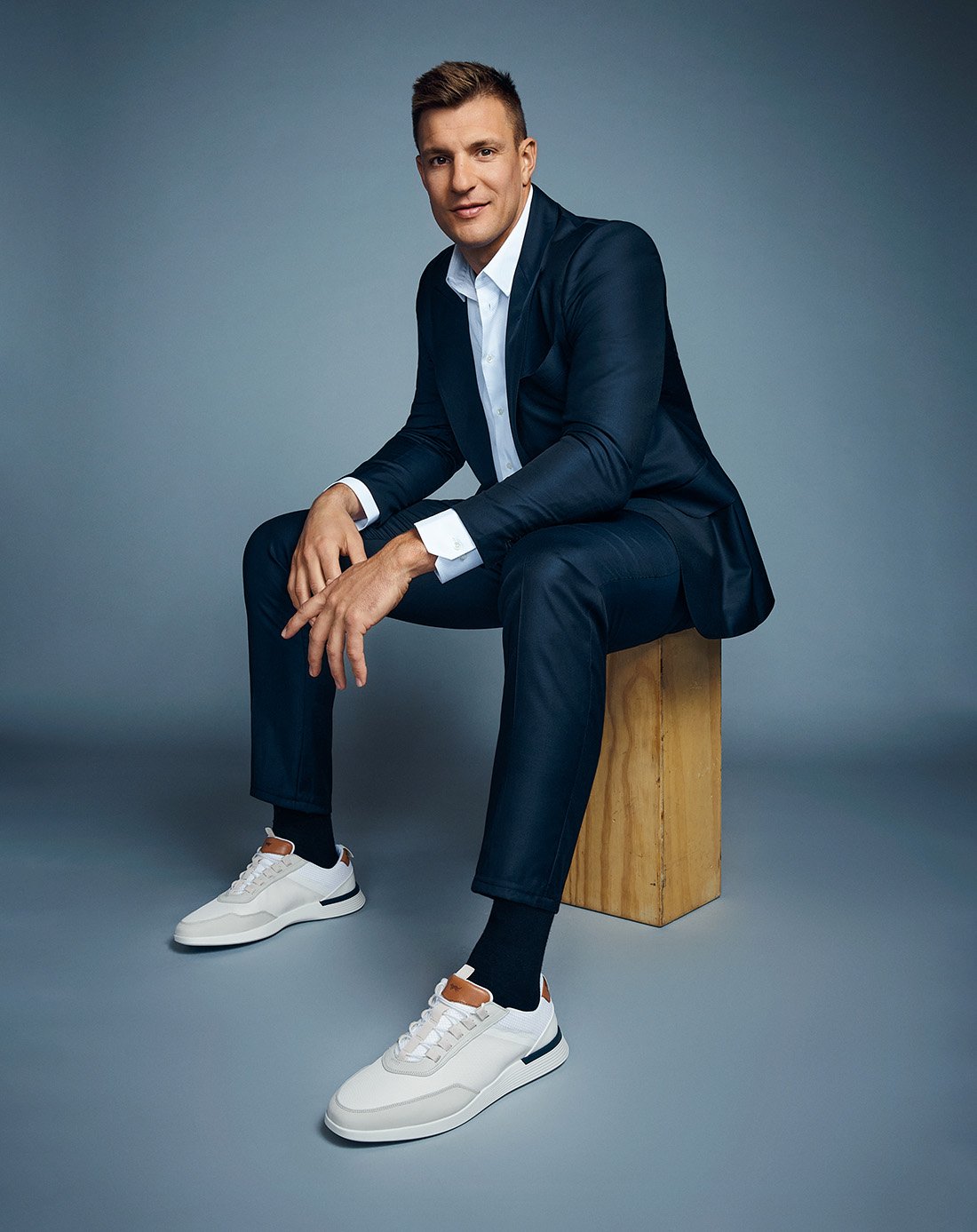 Rob Gronkowski seated on an apple box wearing Crossover Victory Trainer in White/White.