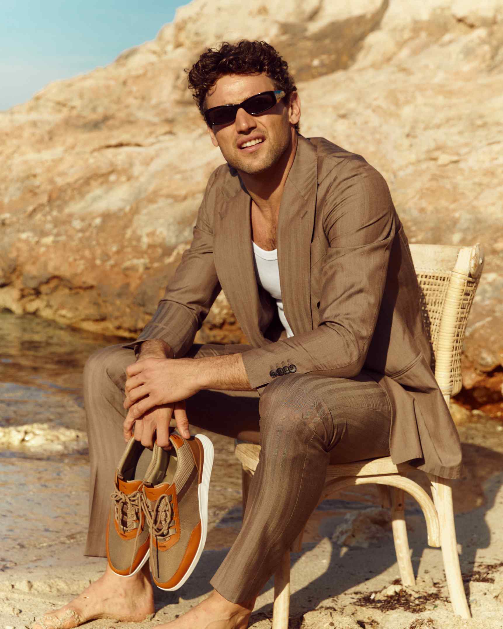 Man sitting on the beach on a chair holding crossover victory trainer in khaki