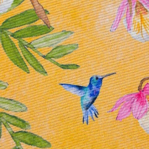 A closeup image of a polyester outdoor rug weave with a vibrant yellow design of tropical birds and foliage.