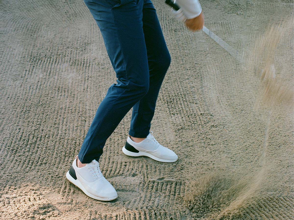 Knee down view of man at a golf course wearing Crossover Golf in Coast White