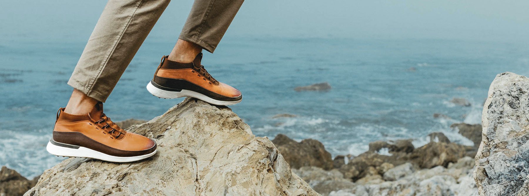 Knee down view of a man walking on a rock wearing Men's Boot Crossover Mid WTZ in Honey with the ocean in the background