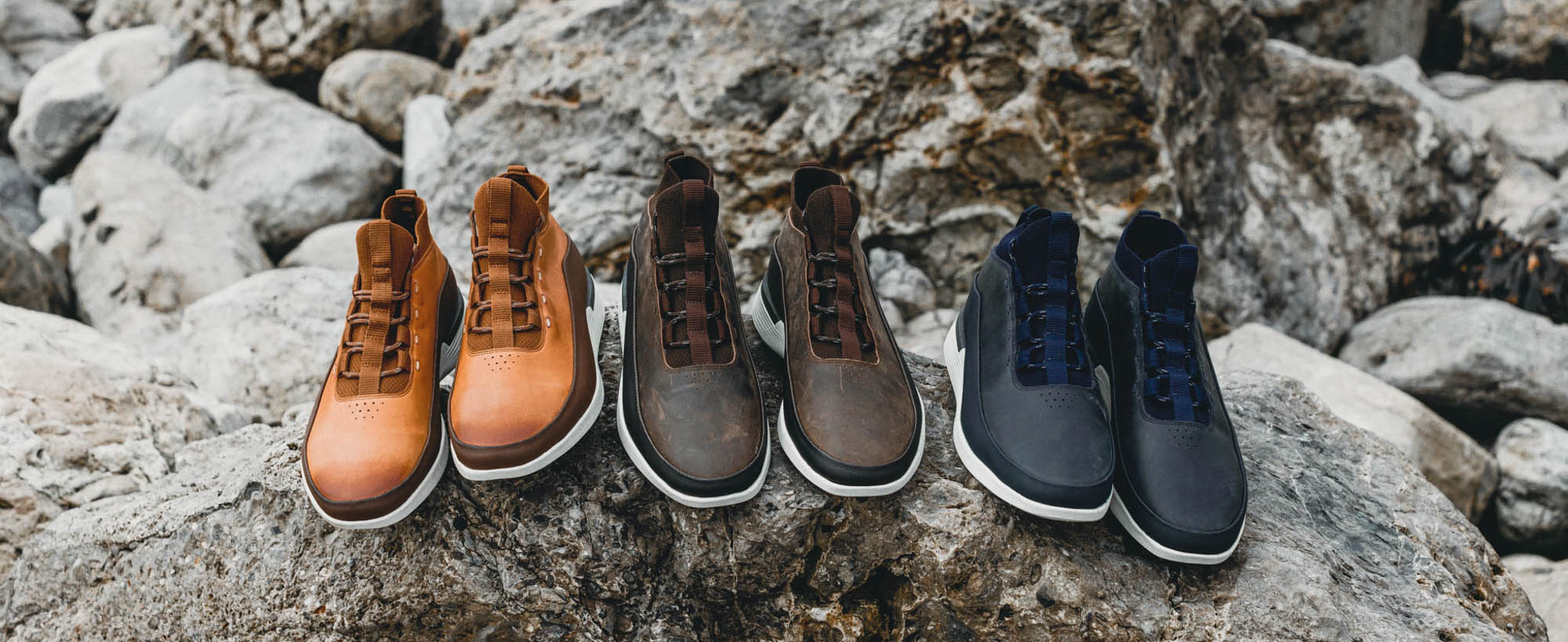 Overhead view of Men's Boot Crossover Mid WTZ in Honey, Brown, and Navy next to one another on a large rock.