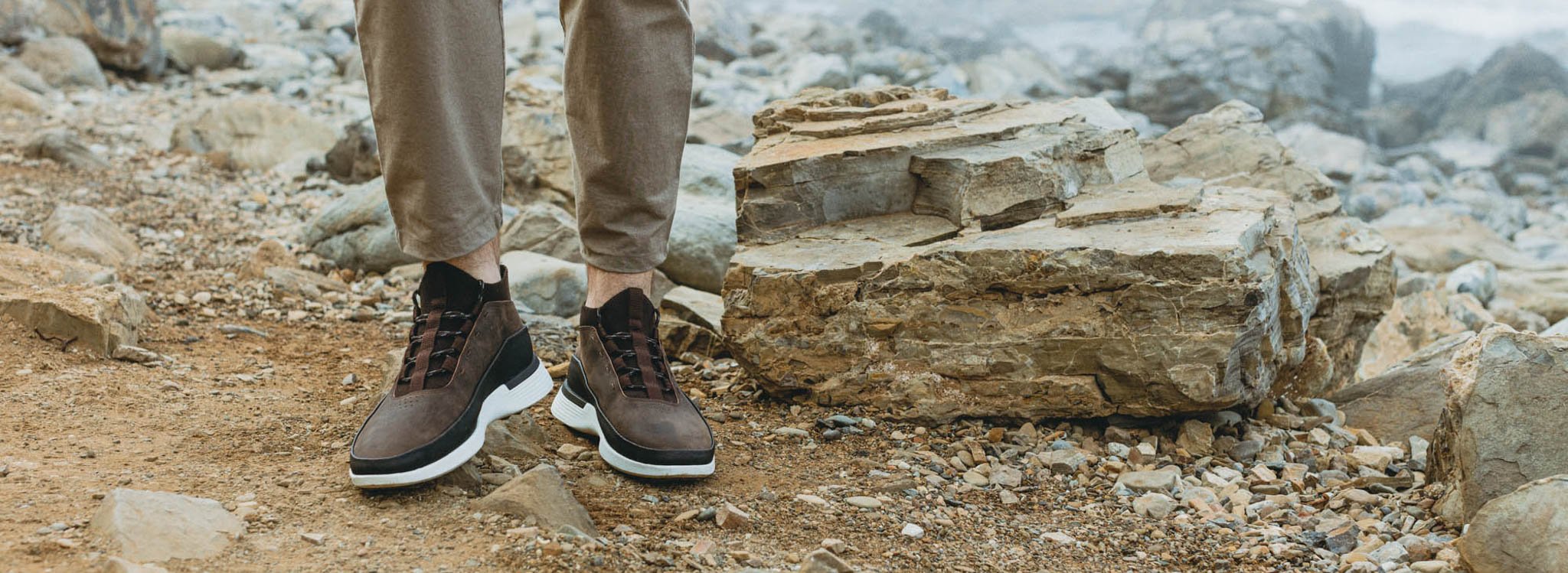 Knee down view of a man wearing Men's boot Crossover Mid WTZ in Brown with large rocks in the background