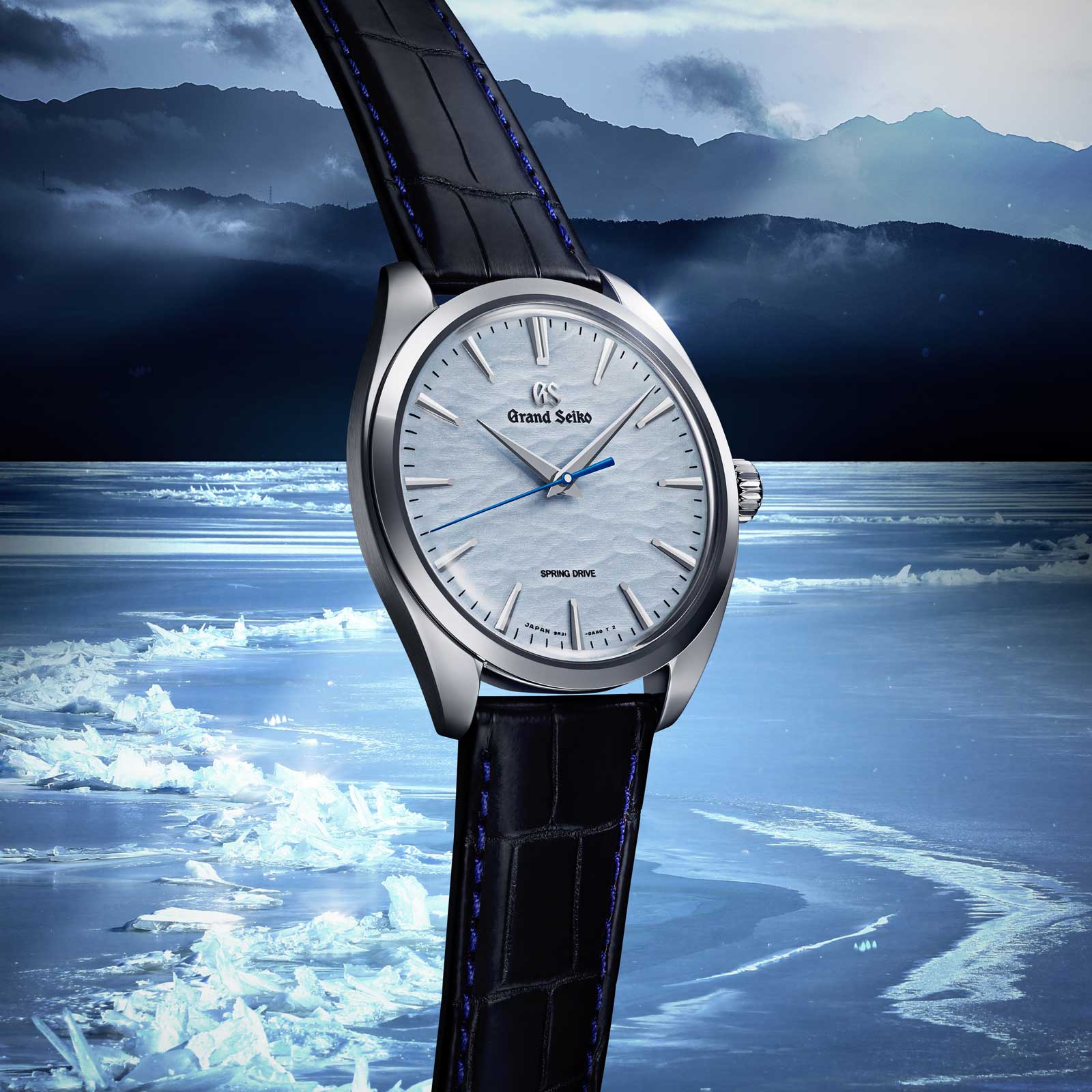 Grand Seiko SBGY007 - blue dial wristwatch in a stainless steel case against frozen lake background. 