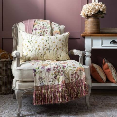 A fringed floral throw and co-ordinating floral cushion arranged on a white armchair among spring and summer decor.