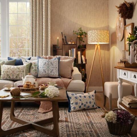 A country style living room decorated with colourful and rustic summer decor, including geometric cushions, floral cushions and a textured throw.