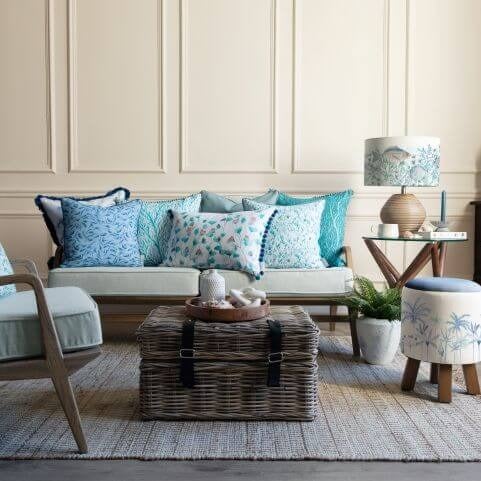 A European style living room decorated with colourful summer decor, including bright blue cushions and a footstool with a tropical design.