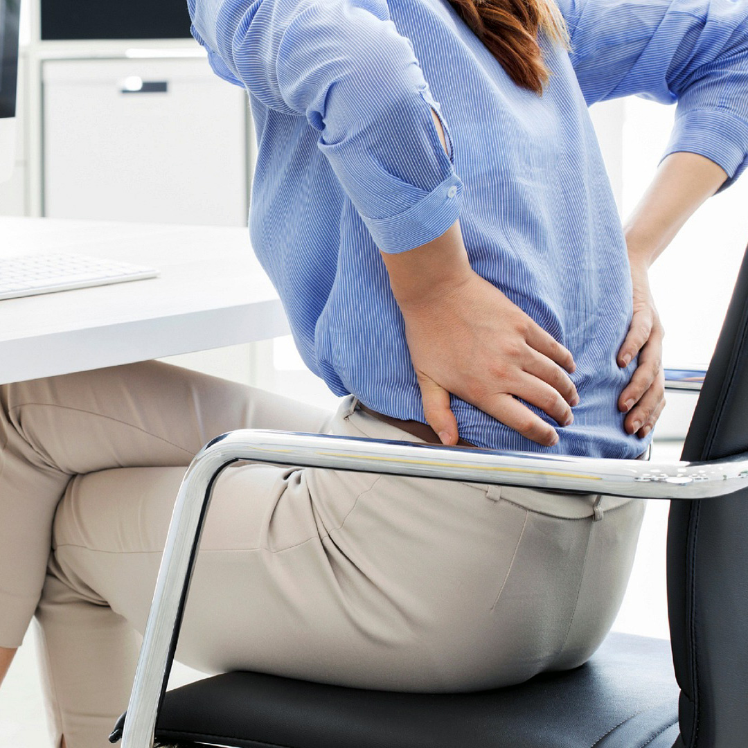 Woman in Office Chair Holding Lower Back From Sciatica Pain.