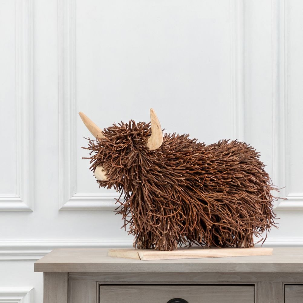 A highland cow sculpture made from renewable wood materials, placed on a wooden coffee table.