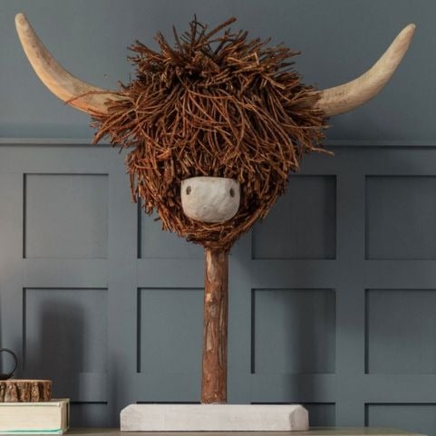 A freestanding highland cow sculpture made using renewable wood materials, placed on a table in front of a deep blue wall.