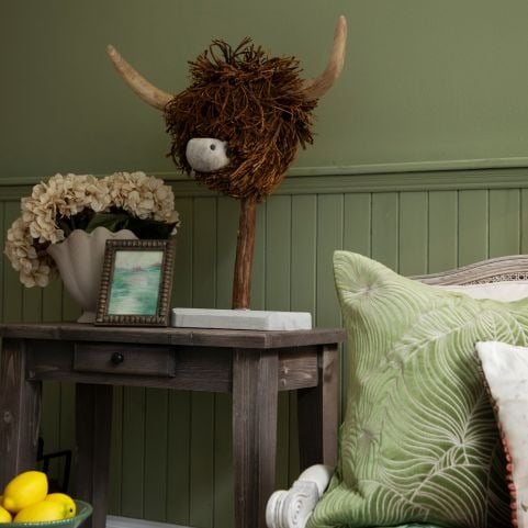 A highland cow ornament placed on a wooden console table with a vase of flowers and a framed photograph.