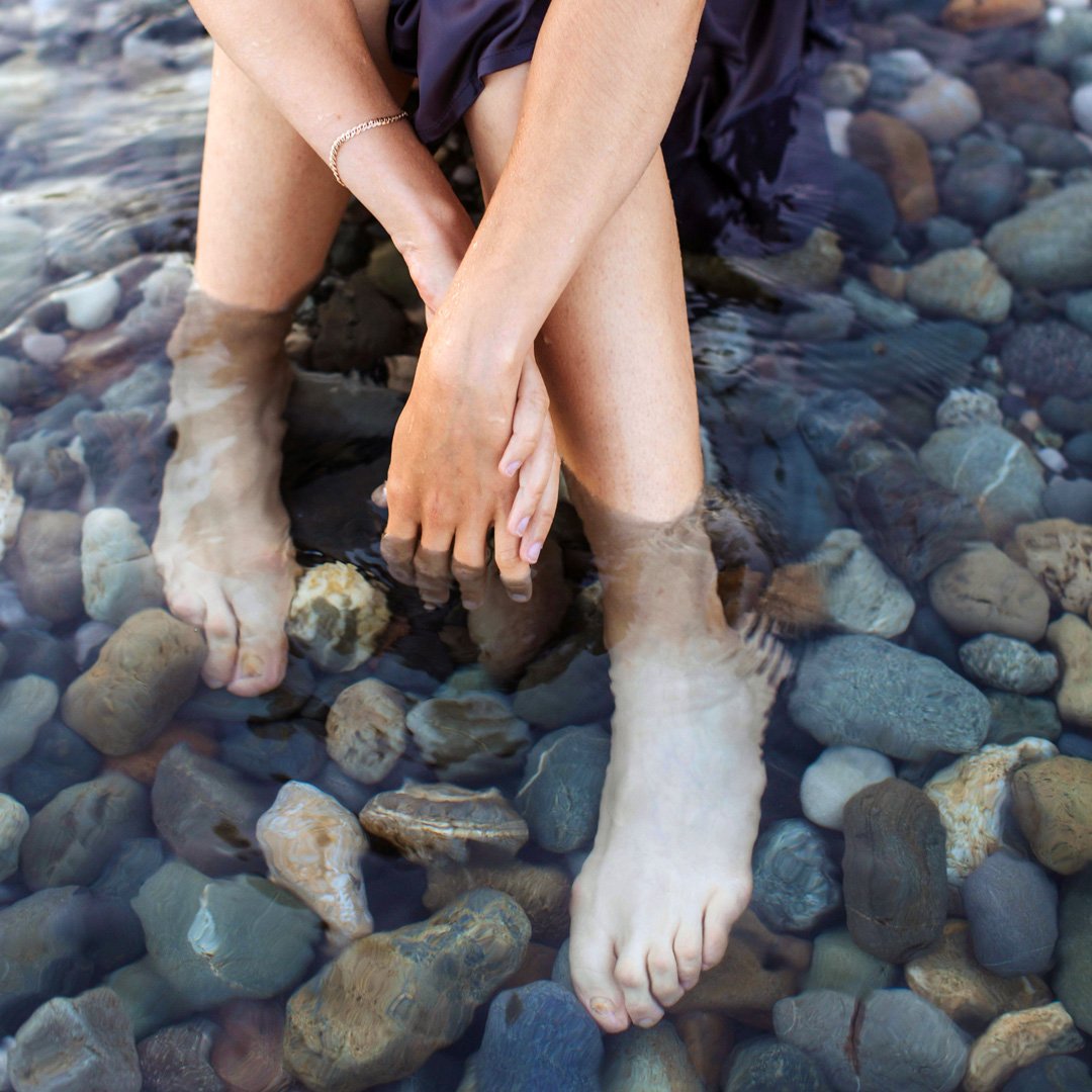 Woman with feet on top of river rocks.