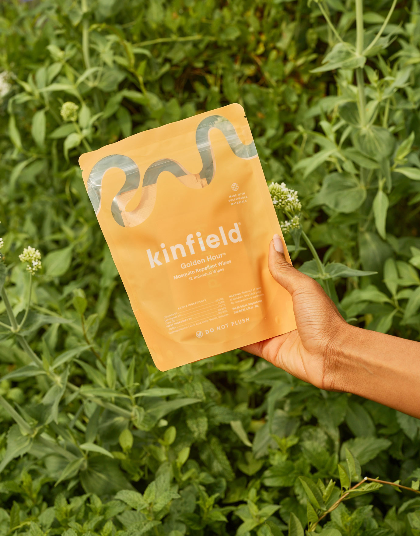 A hand holds a bag of Golden Hour Repellent Wipes in front of green leaves. 